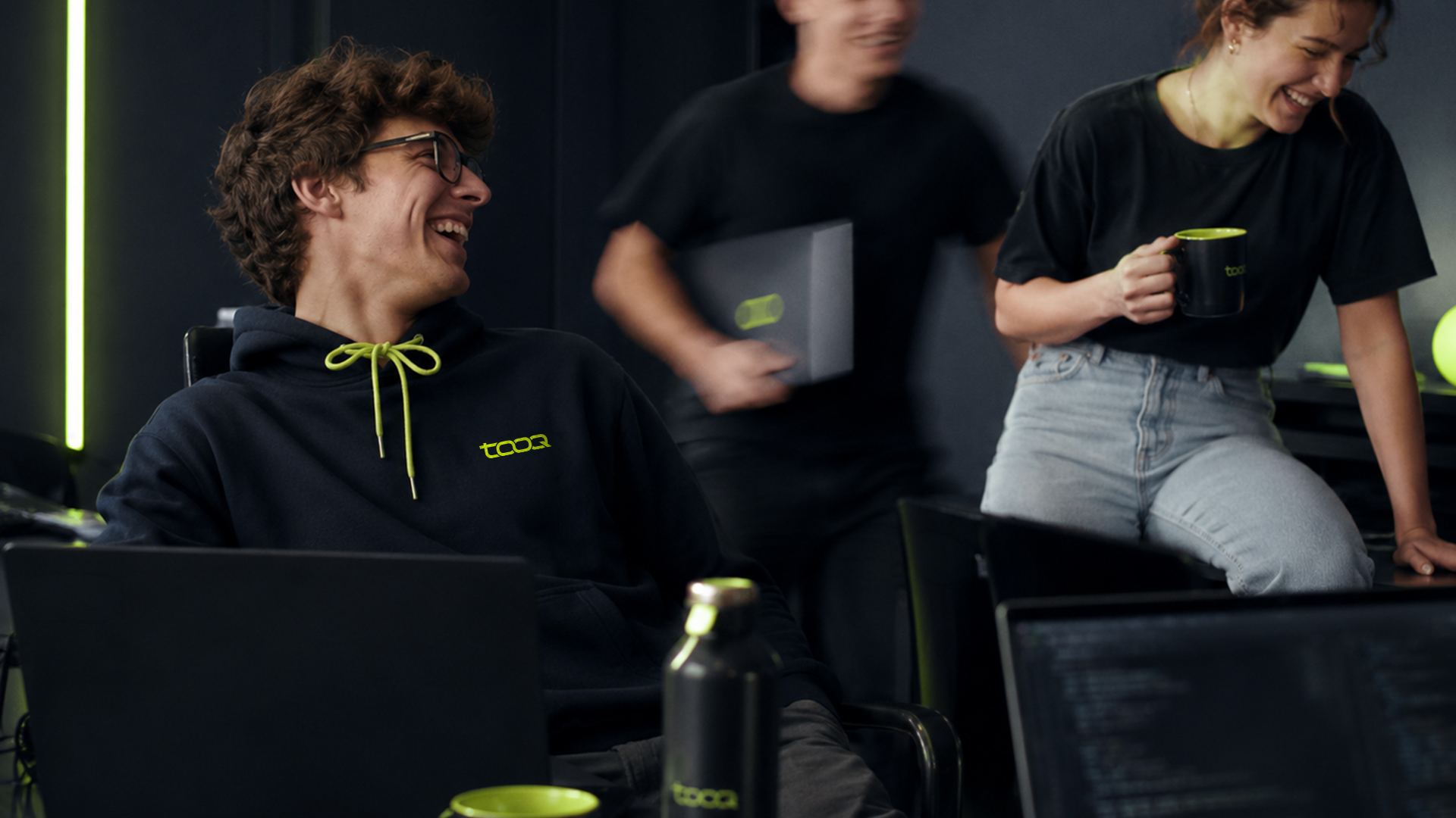 People collaborating in a dark workspace, with Tooq apparel and signal lime details.